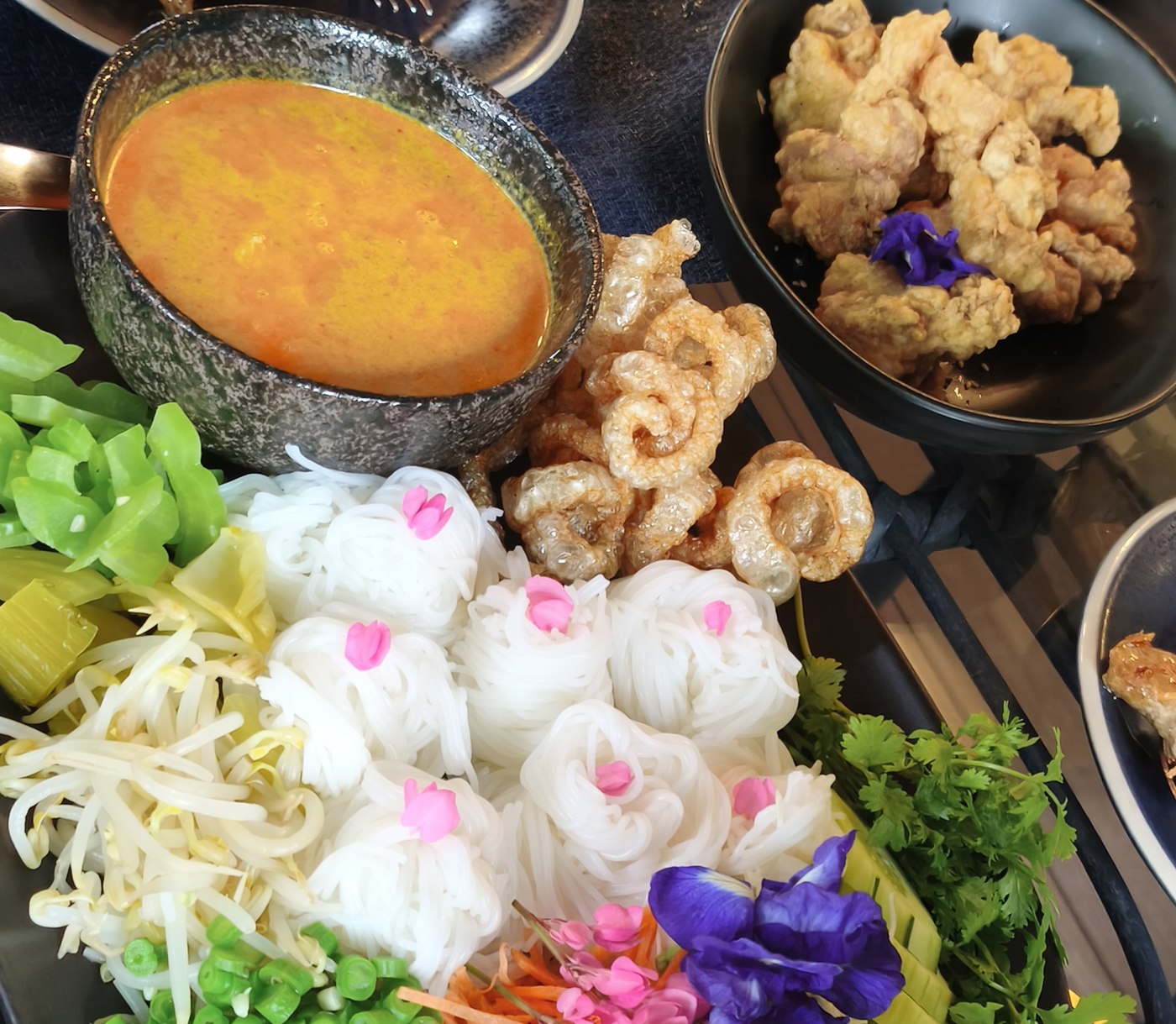 Khanom jeen nam ngiao, a Northern Thai rice noodle dish, served with herbs, curry sauce and edible flowers