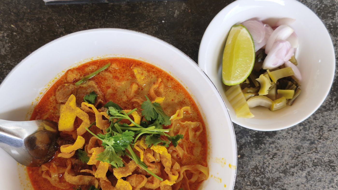 Khao soi, a signature Northern Thai curry noodle soup, served with lime, shallots and pickled mustard greens